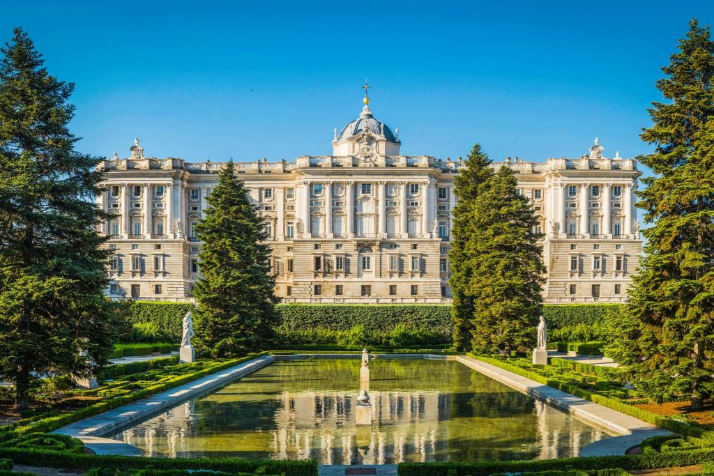잘 꾸며진 정원, 조각상, 반사된 수영장이 있는 돔형 지붕의 웅장한 궁전으로, 맑고 푸른 하늘 아래 자리하고 있습니다.
