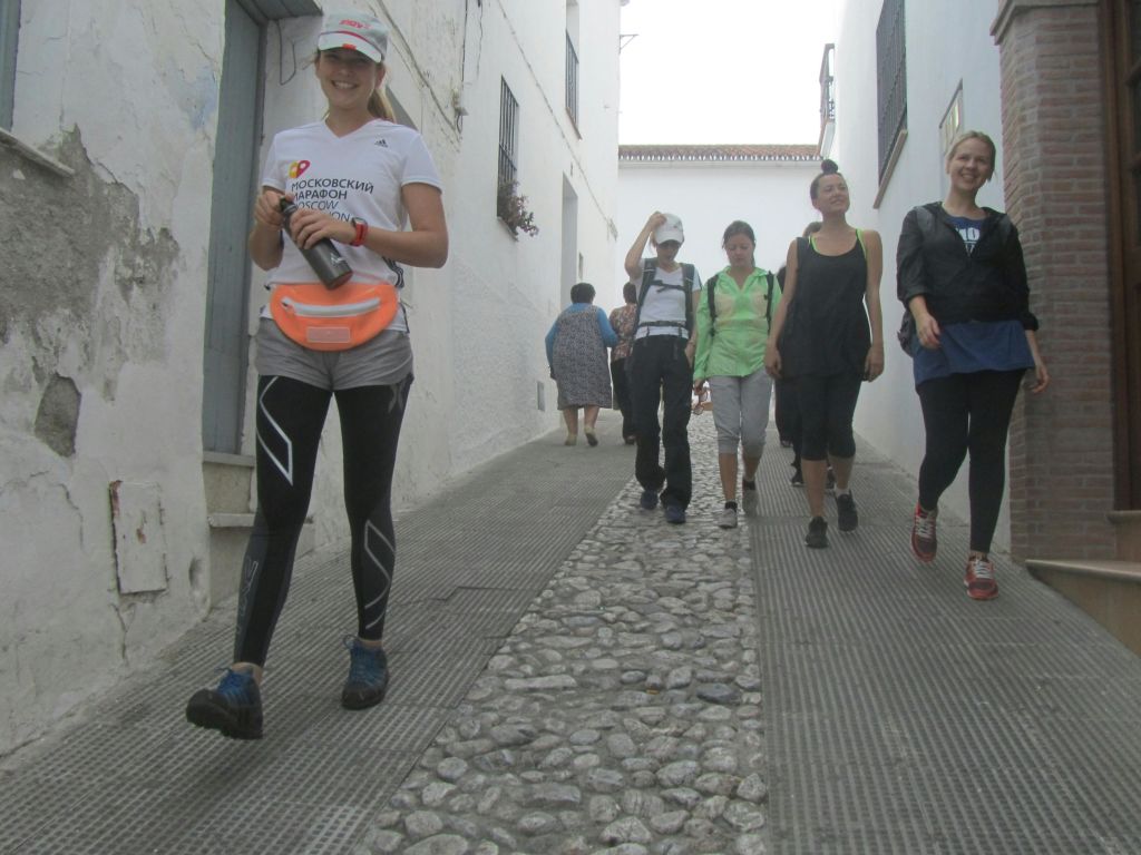 좁고 자갈이 깔린 거리를 걷고 있는 한 무리의 사람들이 하얀 건물과 마주하고 있습니다.