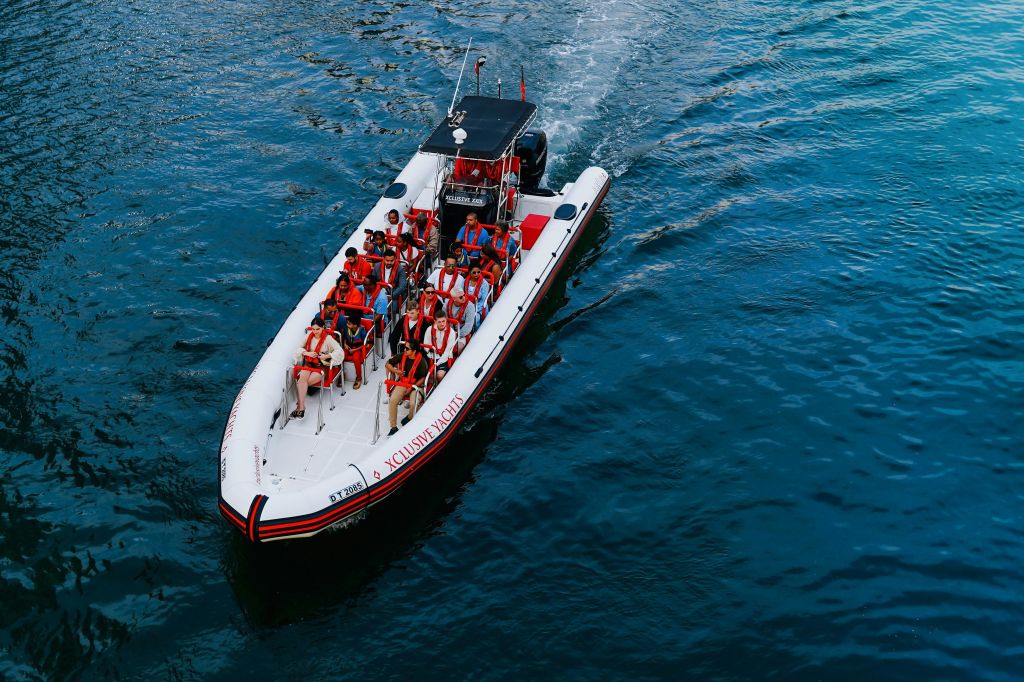 주황색 구명조끼를 입은 여러 사람이 탄 보트가 푸른 바다를 지나고 있습니다.