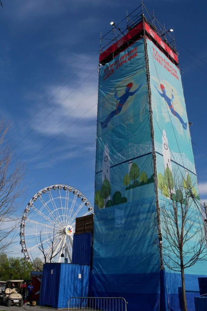 맑고 푸른 하늘 아래 대관람차를 배경으로 집라인 간판과 일러스트가 있는 높은 타워입니다.