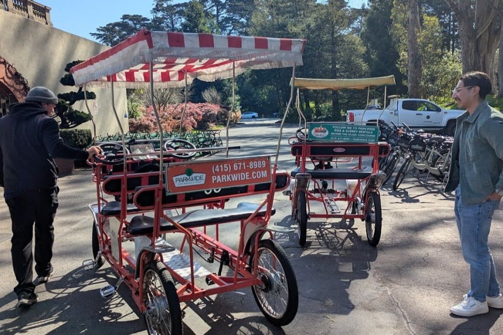 한 남성이 가로수 옆 포장된 공간에 주차된 채 캐노피가 있는 빨간색 자전거 대여소 근처에 서 있습니다.