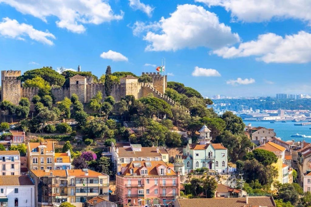 구름이 흩날리는 푸른 하늘 아래 나무와 형형색색의 집들로 둘러싸인 언덕 위의 성.