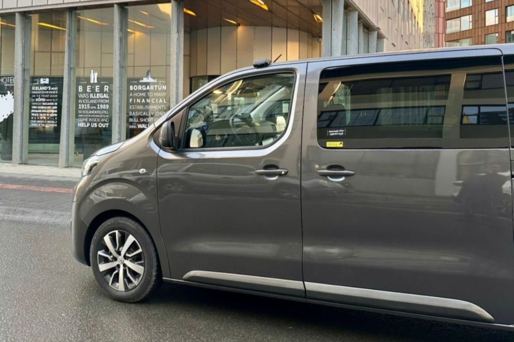 커다란 창문과 문자를 배경으로 한 건물이 있는 거리에 주차된 회색 밴의 측면 모습.