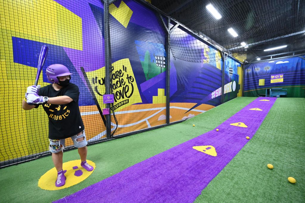 헬멧과 무릎 중괄호를 착용한 사람이 화려한 그라피티가 그려진 활기찬 배팅 케이지에서 박쥐를 잡고 스윙할 준비가 되어 있습니다.