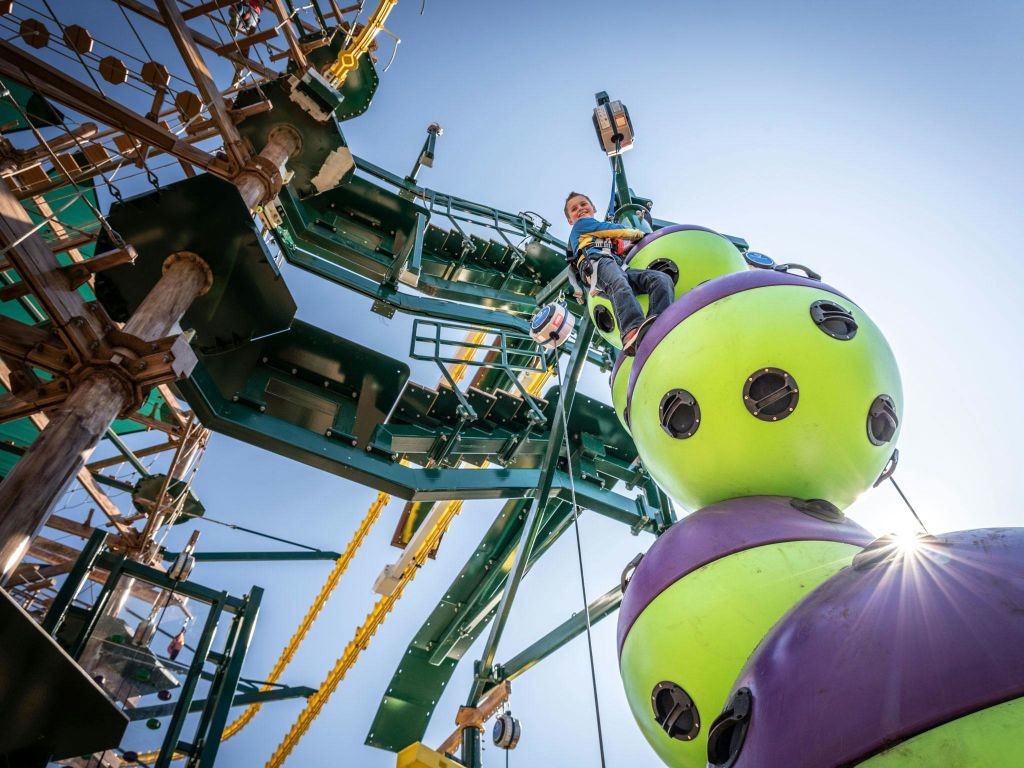 안전 장비를 착용한 사람은 맑은 하늘을 배경으로 녹색 및 보라색 구형 섹션이 있는 다채로운 야외 구조물에 올라갑니다.