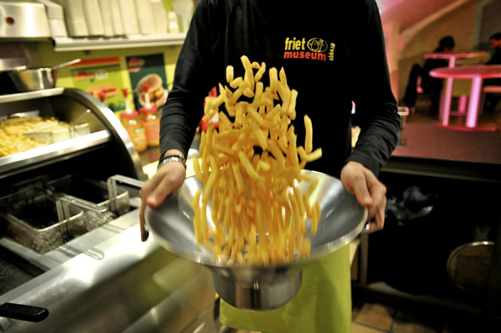 프릿 박물관에서 프렌치 프라이 한 그릇을 버리는 사람. 배경에는 주방 장비와 다채로운 포스터가 포함됩니다.