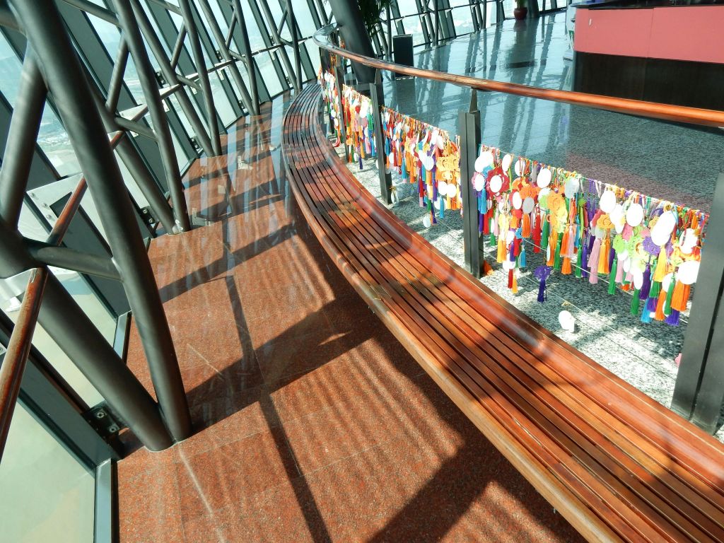 커다란 창문이 있는 현대적인 건물 내부에 화려한 걸이 장식으로 장식된 난간 옆의 곡선형 나무 벤치.