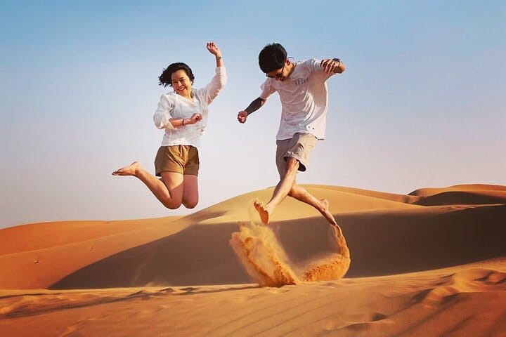 맑고 푸른 하늘을 배경으로 두 사람이 모래 언덕을 기쁘게 뛰어다니고 있습니다.