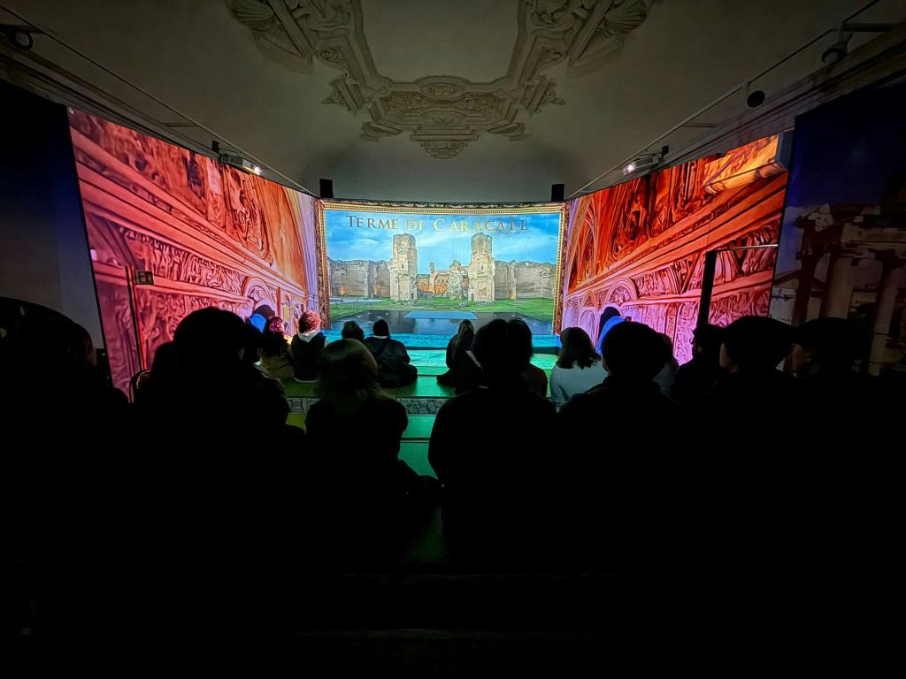 어두운 방에 앉아 건축물과 텍스트가 담긴 역사적인 장면을 감상하는 사람들.