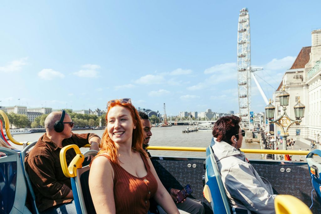 강 전망과 도시 건물을 배경으로 탁 트인 버스를 타고 화창한 하루를 즐기는 사람들이 많습니다.
