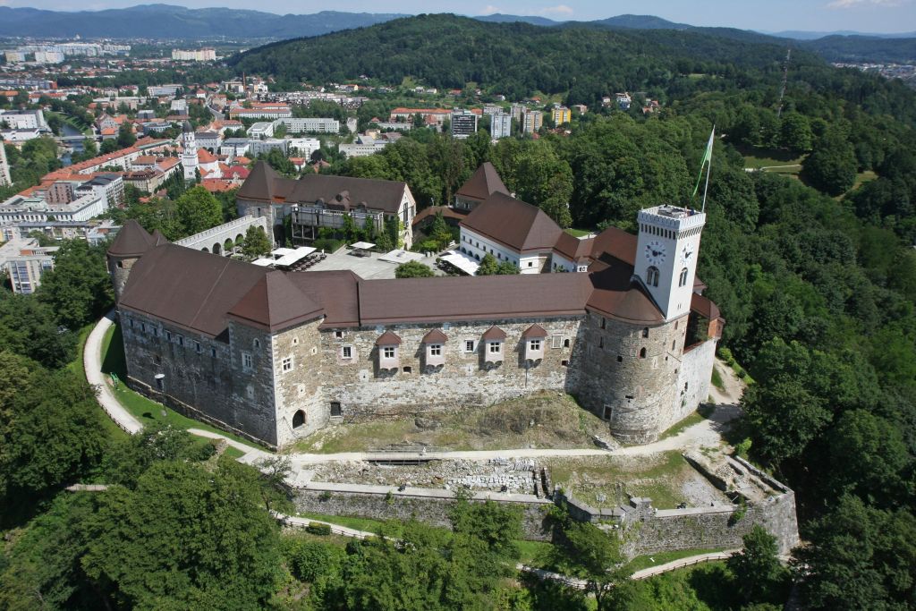 푸르름과 마을을 배경으로 갈색 지붕과 시계탑이 있는 커다란 중세 성의 공중 전망.