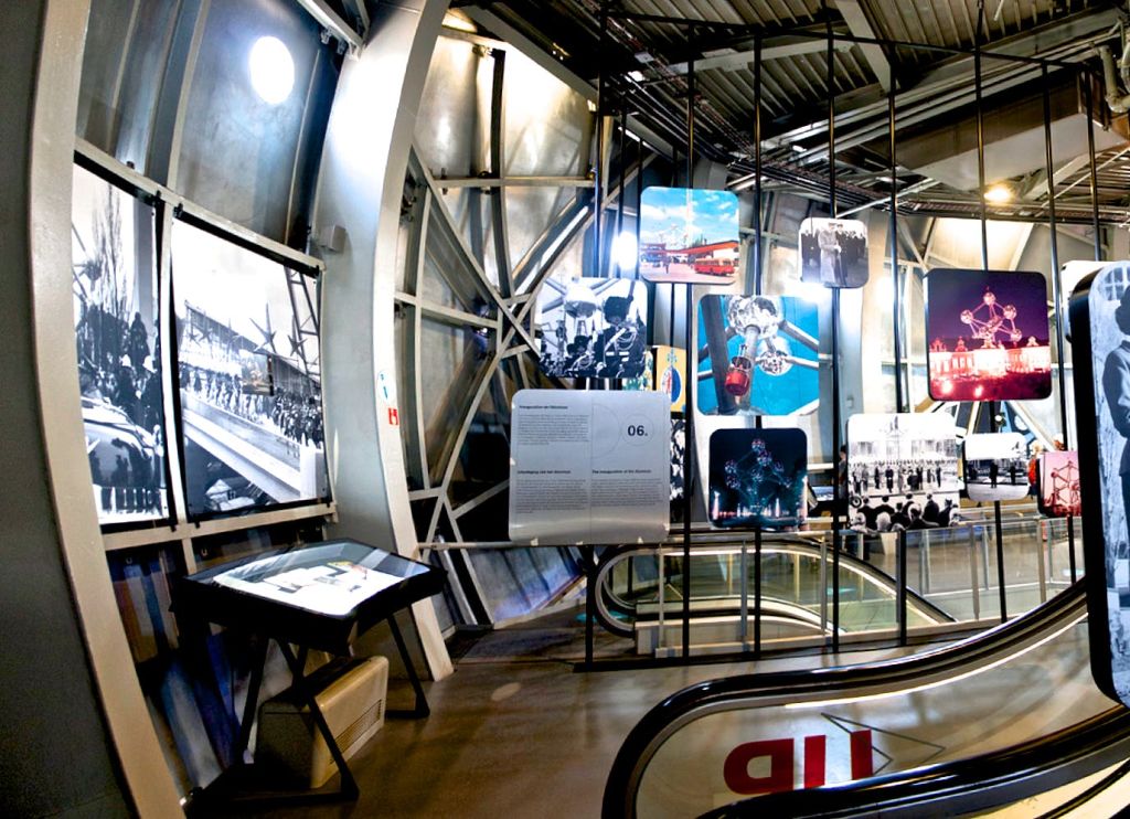 에스컬레이터 근처의 금속 프레임에 다양한 역사 사진과 패널이 전시된 실내 전시물.
