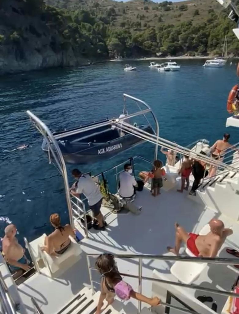 다른 보트와 바위가 많은 해안선을 배경으로 보트 갑판에서 수영복을 입은 사람들.