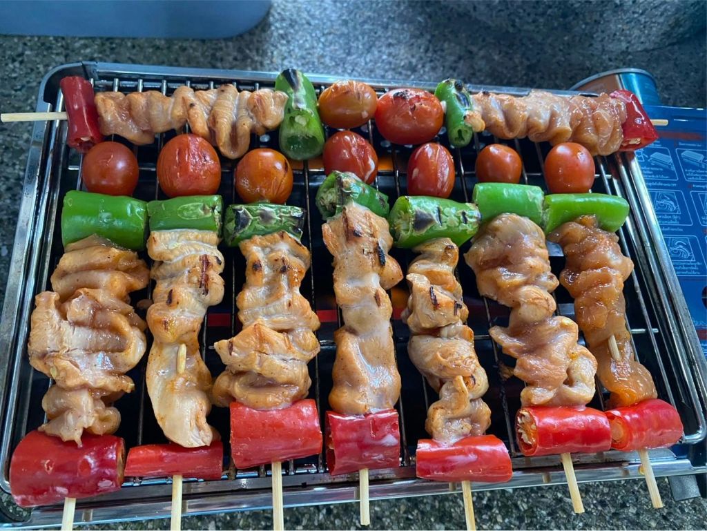 메탈 그레이트에 닭고기, 체리 토마토, 청양고추, 붉은 피망을 얹은 꼬치구이.
