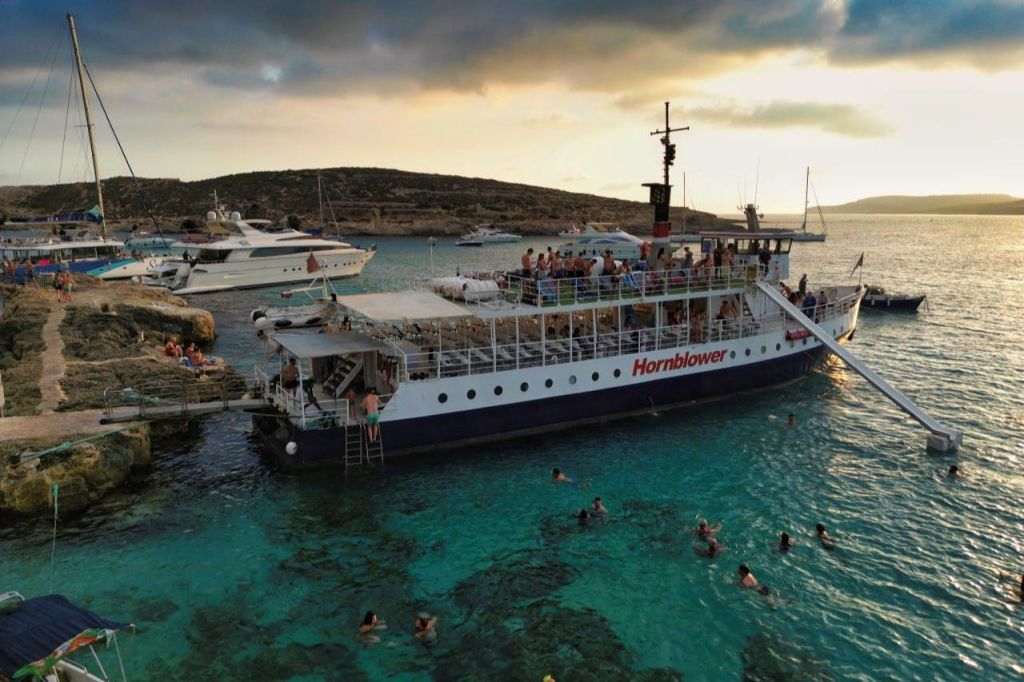 청록색의 맑은 물에 정박한 '혼블로어' 라는 이름의 보트에는 근처에서 수영을 즐기고 언덕을 배경으로 사람들의 발길이 이어지고 있습니다.