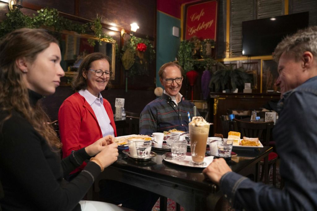 세 사람이 카페 테이블에 앉아 음식과 음료를 즐기고, 축제 인테리어로 둘러싸여 함께 시간을 보내고 있습니다.