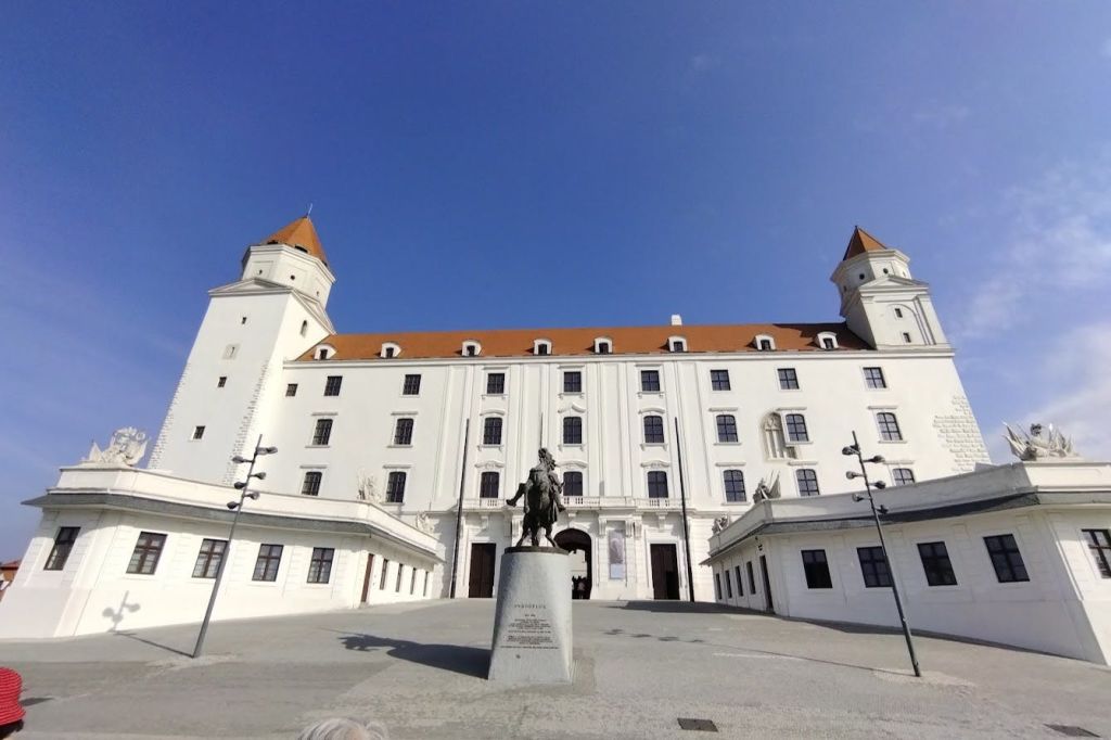 빨간색 지붕이 있는 커다란 흰색 성, 4개의 탑, 승마 동상을 중심으로 한 안뜰, 맑고 푸른 하늘 아래.