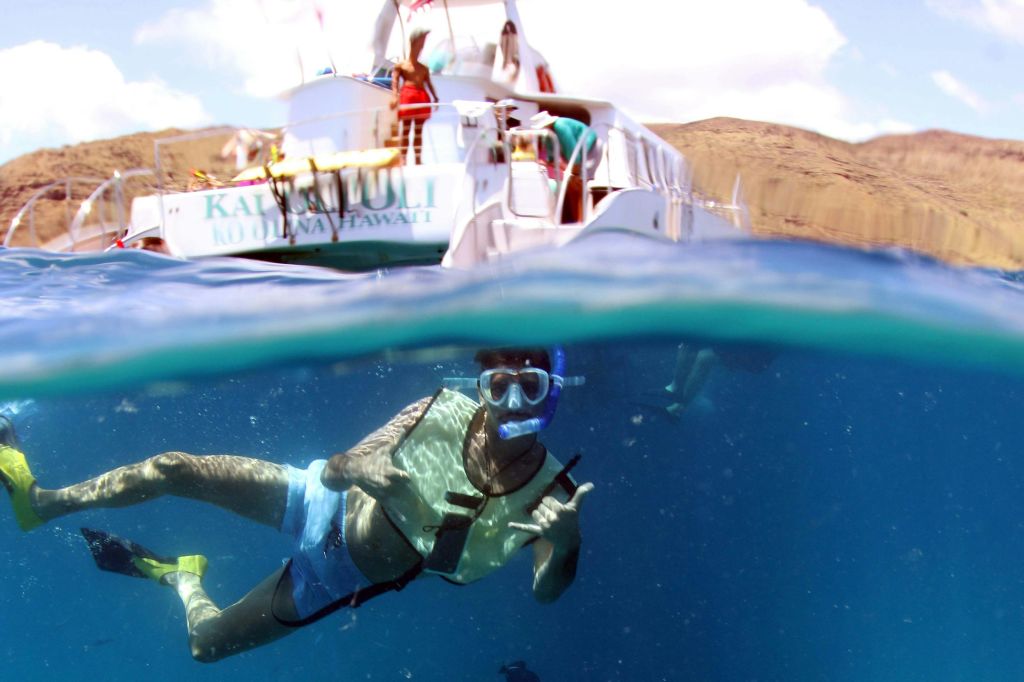 맑은 하늘과 바위 풍경을 배경으로 사람들이 탑승한 보트 근처에서 스노클링을 즐기는 사람.