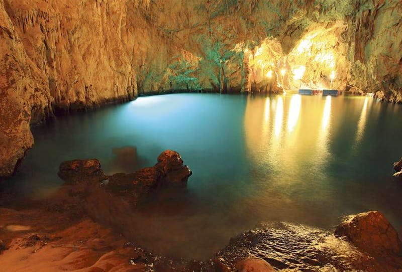 반사되는 푸른 물이 흐르는 지하 동굴 수영장에서 따뜻한 조명으로 조명을 받으며 험준한 암벽을 감상할 수 있습니다.