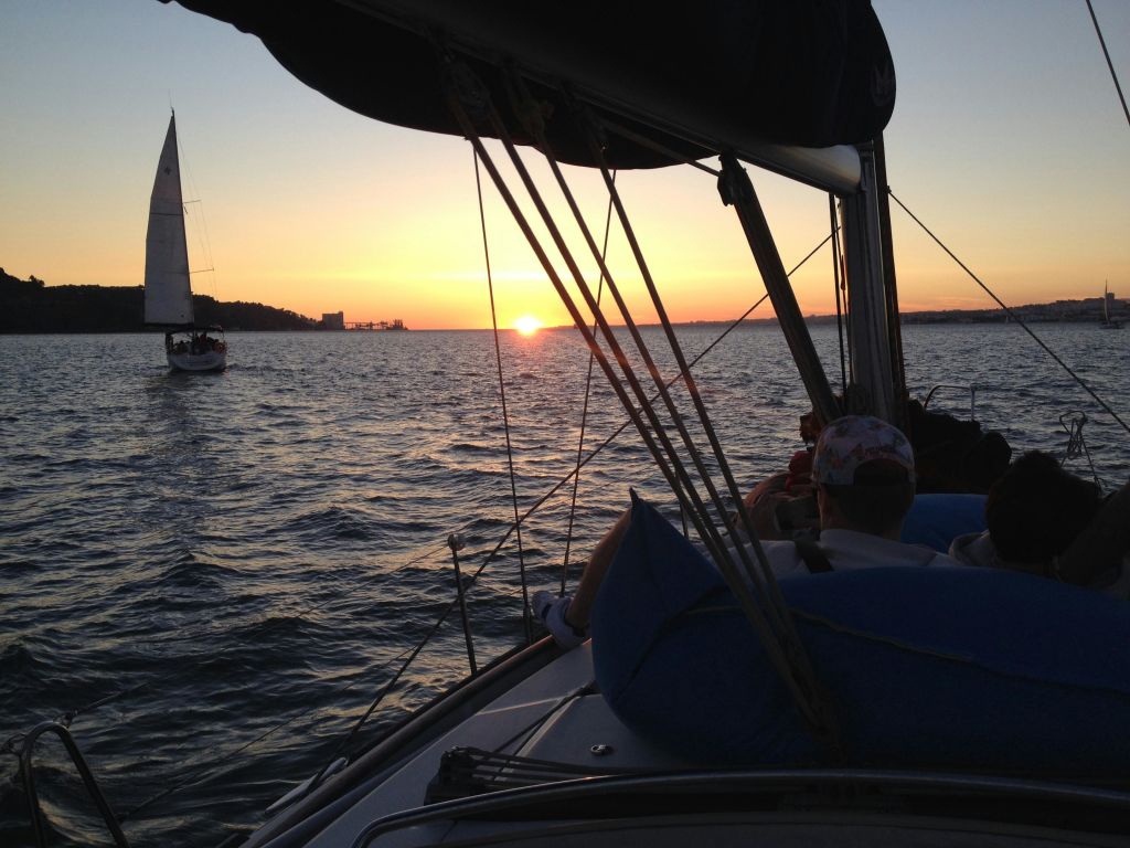 일몰에 요트를 타고 멀리 보이는 또 다른 요트와 함께 사람들이 잔잔한 물 위에서 보트를 타고 있습니다.