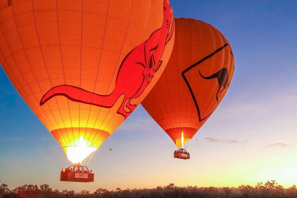 캥거루 디자인이 돋보이는 두 개의 열기구가 해가 지는 동안 풍경 위에 떠 있습니다.