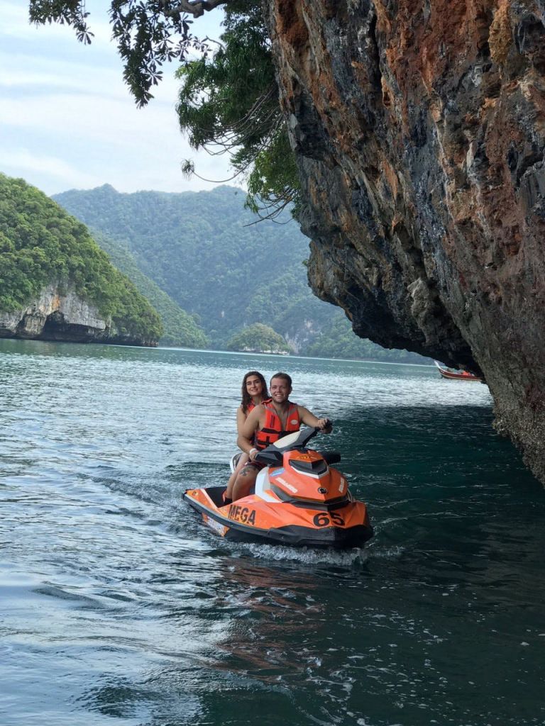 울창한 푸른 언덕을 배경으로 잔잔한 바위 절벽 근처에서 제트 스키를 타는 두 사람.