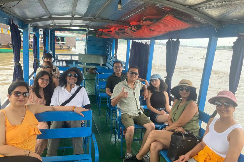 한 무리의 사람들이 강가에서 열린 보트를 타고 푸른 벤치에 앉아 미소를 짓고 있습니다. 모자와 선글라스를 착용하는 사람도 있습니다.