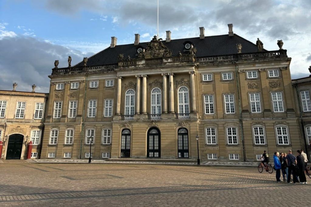 기둥과 조각상이 있는 크고 화려한 건물로 많은 창문과 타일 지붕이 있으며 맑은 날 구름이 보입니다.