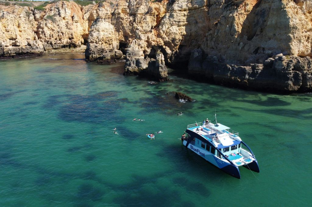 '블루 플리트 (Blue Fleet)' 라는 이름의 보트가 바위 절벽을 배경으로 맑고 푸른 바다를 헤엄치고 있습니다.