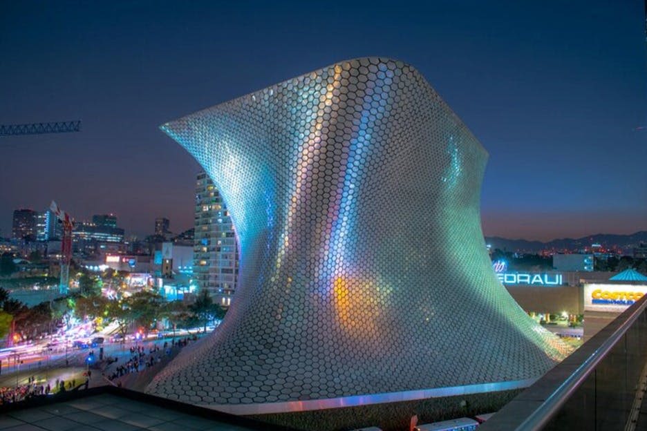 활기찬 도시 풍경 속에서 야간 조명을 받으며 육각형 타일 외관이 반전된 미래 지향적인 건물입니다.