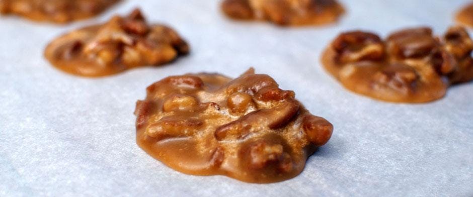 흰색 표면에 피칸 프랄린을 클로즈업하여 광택 있는 카라멜 코팅과 눈에 띄는 너트 텍스처가 특징입니다.