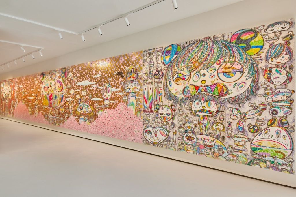 흰색 갤러리 벽에 추상적이고 만화 같은 인물과 패턴이 스포트라이트 아래 표시된 다채로운 벽화입니다.