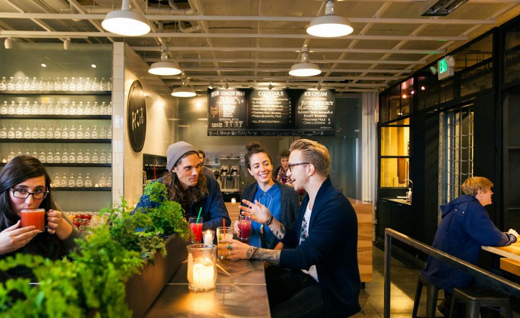 4명의 일행이 바에 앉아 밝고 현대적인 분위기에서 음료를 즐기고 대화를 나눕니다.