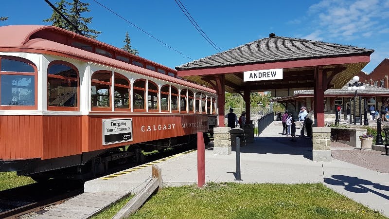 "ANDREW" 표지판이 있는 역에서 "CALGARY MUNICIPAL" 라고 표시된 빨간색 열차. 여러 사람이 플랫폼에 있습니다.