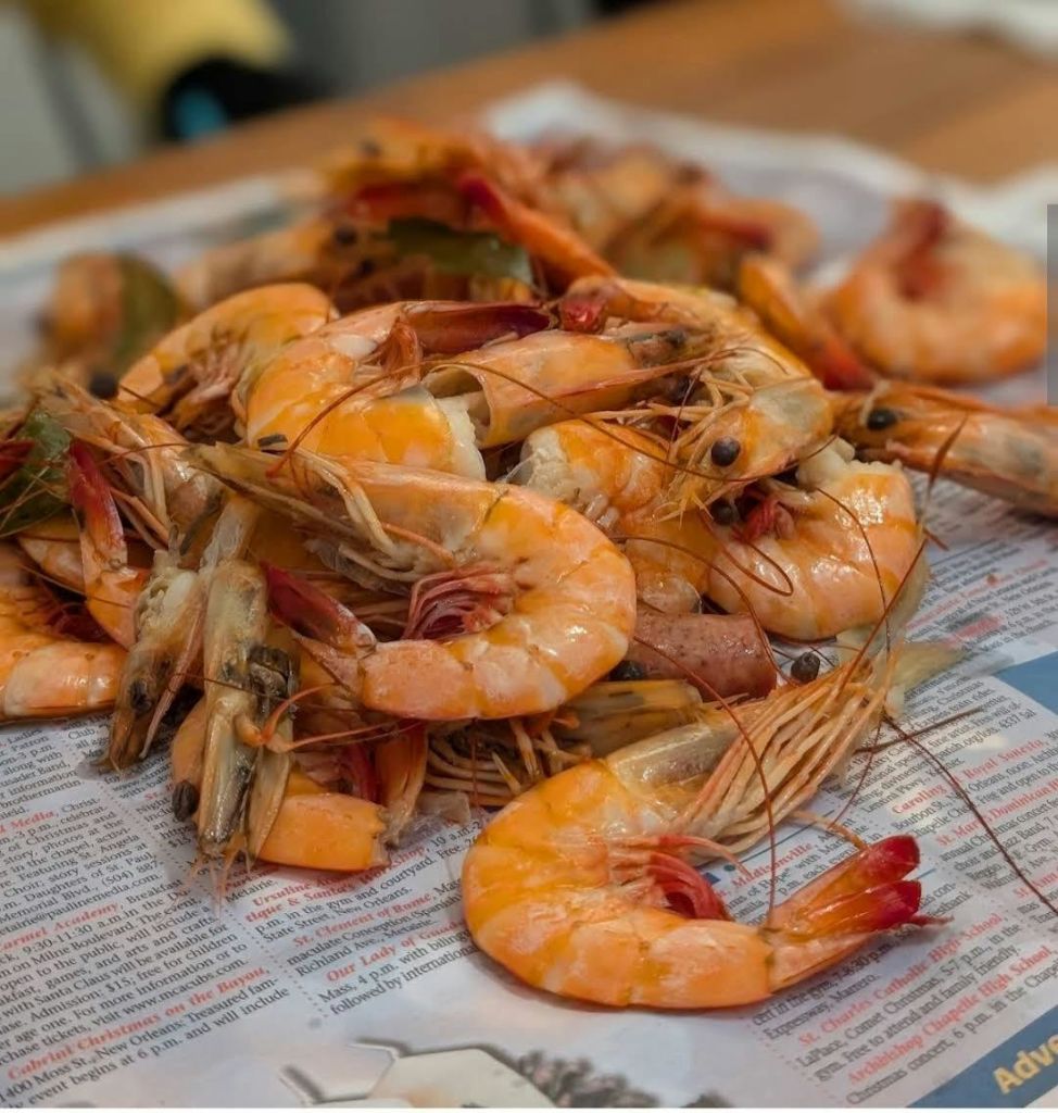 조개 껍질과 머리가 그대로 있는 조리된 새우 더미가 배경이 흐릿한 신문에 놓여 있습니다.