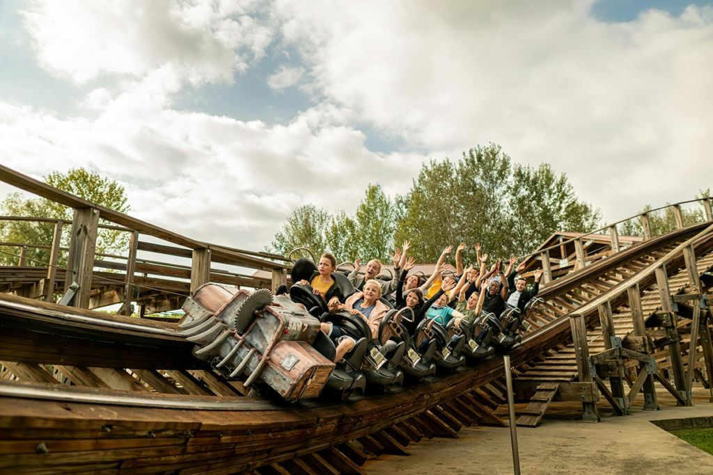 나무와 흐린 하늘에 둘러싸인 채 두 팔을 들어 올린 채 나무 롤러코스터를 타는 사람들.