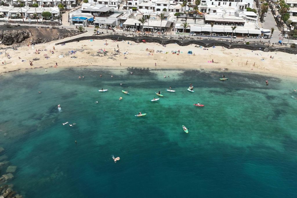 하얀 건물을 배경으로 모래 해변 근처에서 청록색 바다에서 패들보딩과 수영을 즐겨보세요.