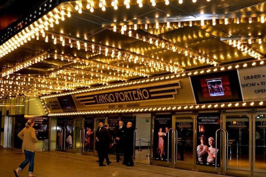"Tango Porteño" 간판, 댄서 포스터, 정장 차림의 사람들이 밖에 서 있는 극장 입구에 조명이 켜져 있습니다.