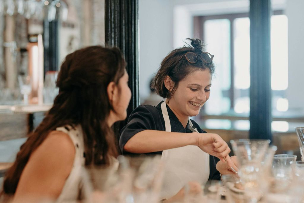 실내 환경의 두 여성, 한 여성은 음식을 흔들며 앞치마를 착용하고 미소를 짓고 요리 활동에 참여합니다.