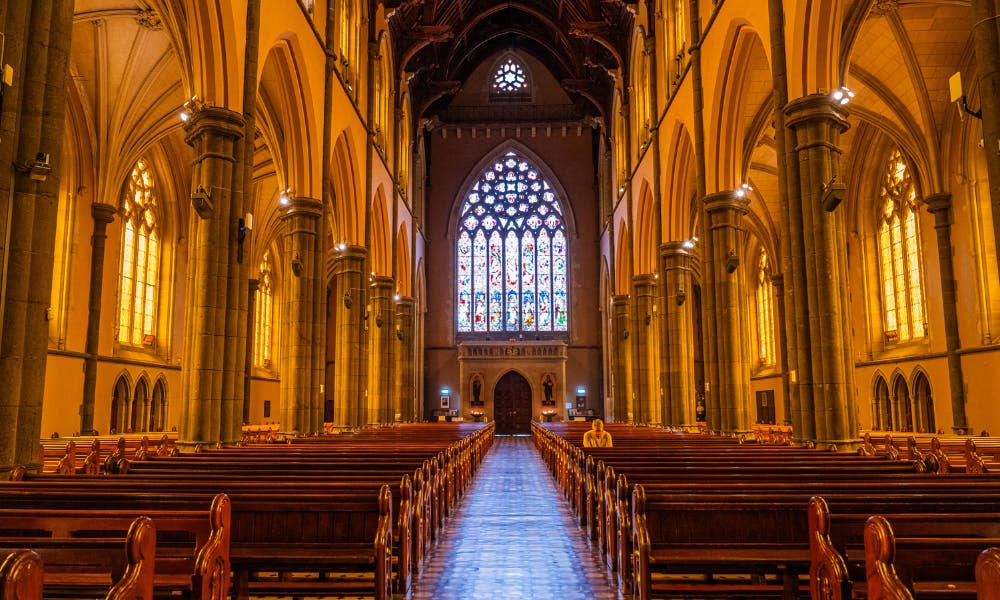 스테인드글라스 창문이 있는 대성당의 내부, 목조 페우, 높은 아치, 정면 근처에 앉아 있는 한 사람.