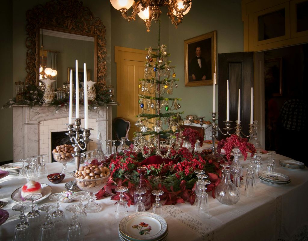 장식된 크리스마스 트리 센터피스, 칸델라브라, 유리 제품, 축제용 화환을 테이블에 놓은 우아한 다이닝 룸.