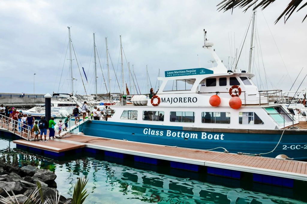 '마조레로' 라는 이름의 파란색과 흰색 유리 바닥 보트가 선착장에 정박해 있으며, 나무 부두에서 사람들이 승선하고 있습니다.