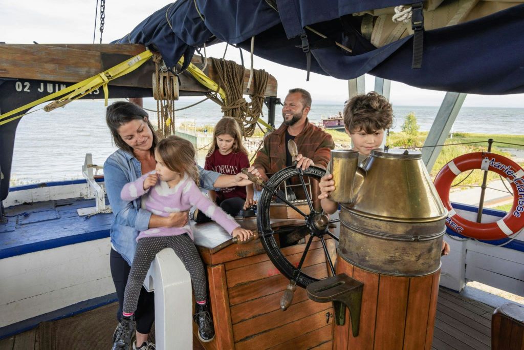 한 명의 남자와 세 명의 어린이가 한 명의 어린이가 조종하는 보트의 조종석에 있습니다. 인생 반지에는 '애틀랜틱 크루즈' 라고 쓰여 있습니다. 백그라운드에서 바다를 볼 수 있습니다.