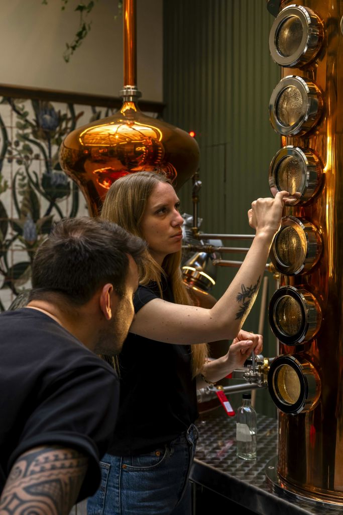 작업장 같은 환경에서 유리로 된 관측 포트가 있는 구리 증류 장치를 검사하는 두 사람.