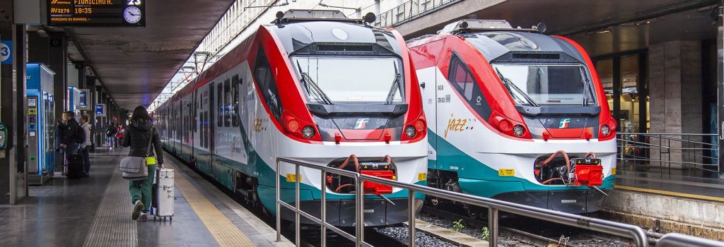 빨간색과 흰색 간판이 나란히 선로에 주차되어 있고 부분적으로 플랫폼 난간으로 덮여 있는 두 개의 현대적인 열차의 전면 모습.