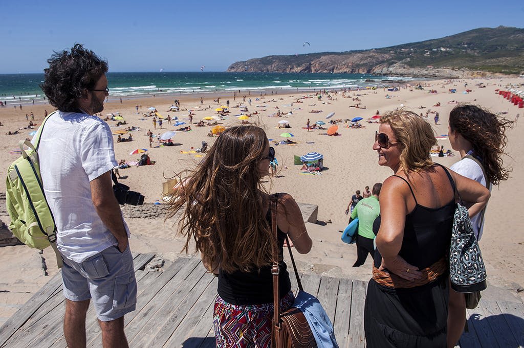 바다 근처에 우산과 일광욕을 즐길 수 있는 붐비는 모래 해변이 내려다보이는 나무 플랫폼에 서 있는 두 사람.