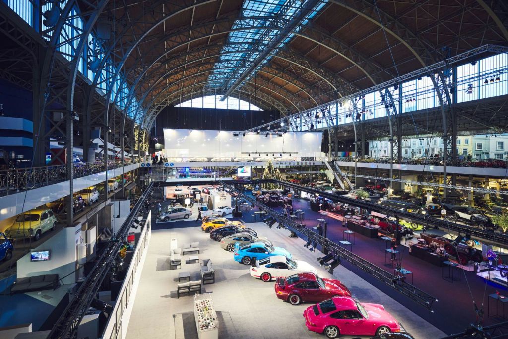 스포츠카가 전시된 전시장에는 밝은 조명, 높은 아치형 천장, 바닥에 다양한 전시물이 있습니다.