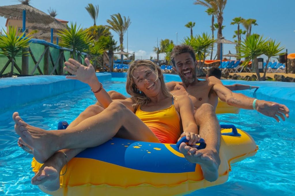 야자수와 라운지 의자로 둘러싸인 수영장의 파란색과 노란색 팽창식 튜브에서 미소를 짓고 휴식을 취하는 남성과 여성.