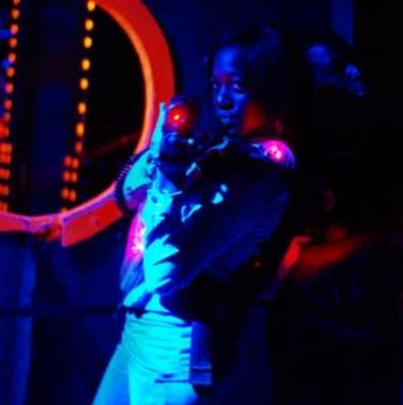 어두운 네온 조명 경기장에서 레이저 태그 건을 조준하는 빛나는 장비를 착용한 사람.