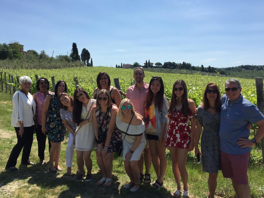 구불구불한 언덕과 맑고 푸른 하늘을 배경으로 포도원 앞에서 사진 촬영을 위해 포즈를 취하고 있는 한 무리의 사람들.